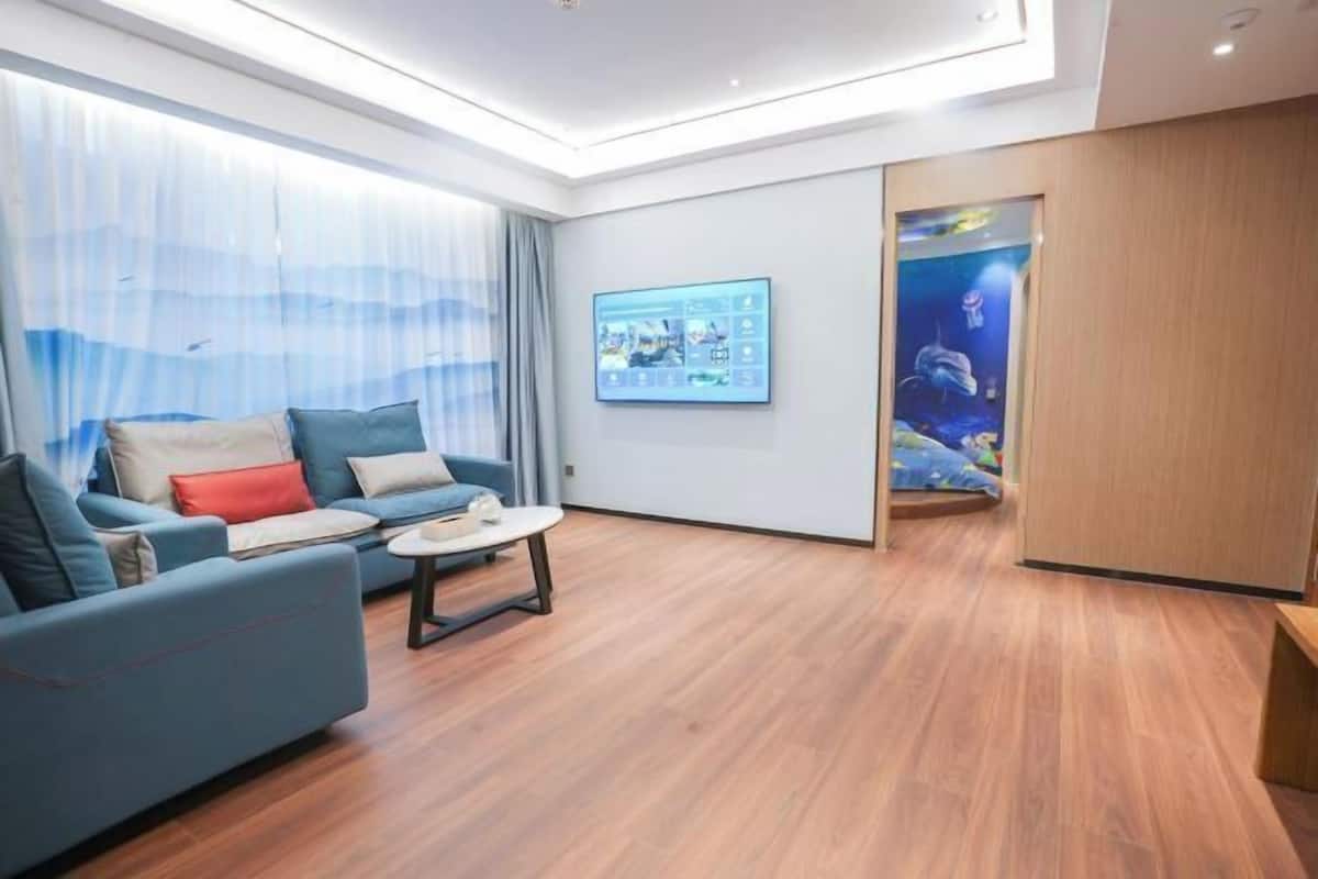 A modern living room with a blue sofa, a small round table, and a large digital display on the wall.