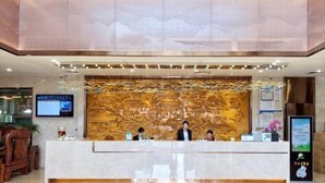 A reception area with a marble counter, a large decorative wall, and a digital screen above the counter. - Shibazi Hotel (Yangjiang)