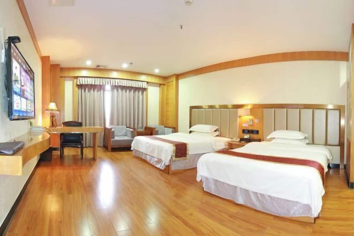 A hotel room with two beds, a desk, a chair, a TV, and a large window with curtains.