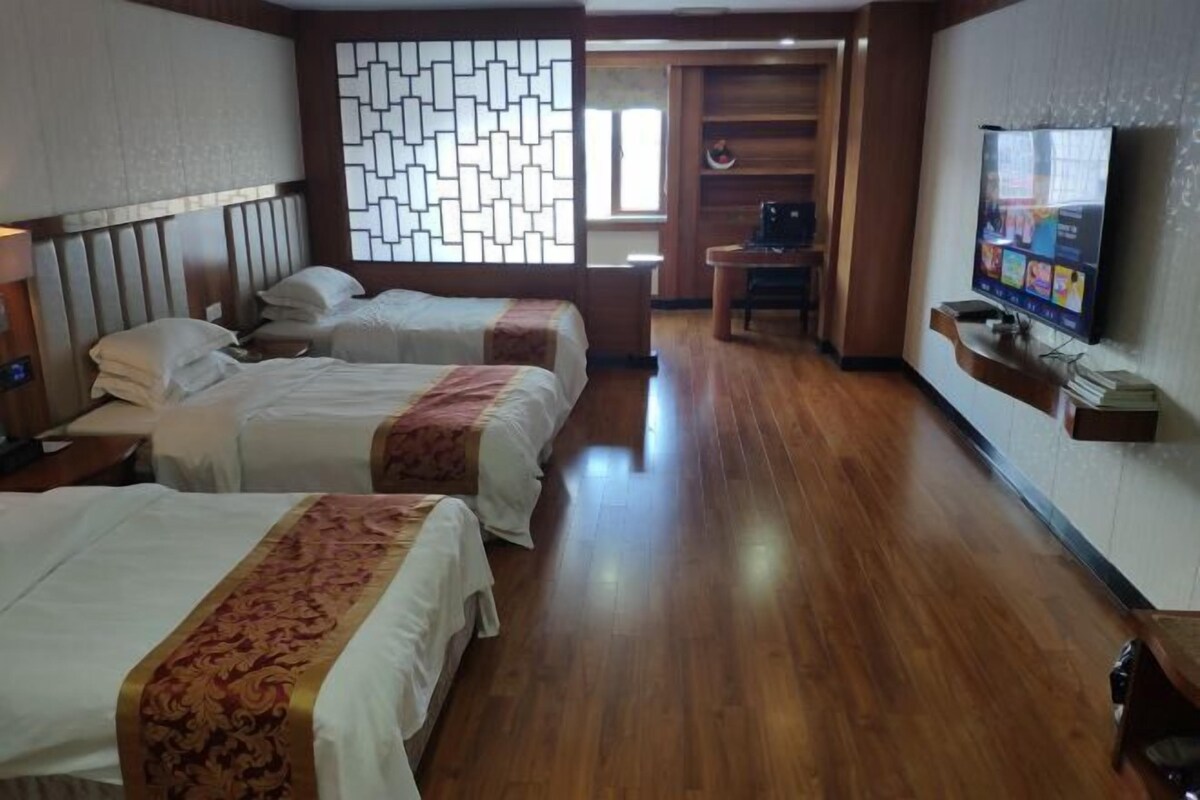 Habitación de hotel con dos camas, televisión, escritorio y suelo de madera.
