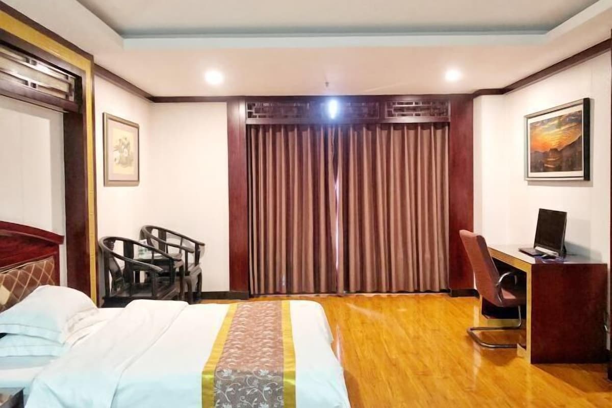 Una habitación de hotel con cama, escritorio, silla, cortina y un cuadro en la pared.