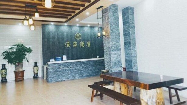 A reception area with a stone wall, wooden ceiling, and a reception desk. - Tangquan Mingwu Hostel (Xiamen)