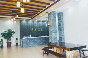 A reception area with a stone wall, wooden ceiling, and a reception desk. - Tangquan Mingwu Hostel (Xiamen)