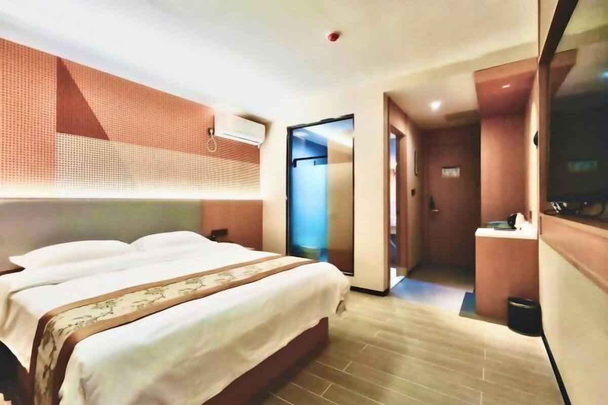 Habitación de hotel con cama, televisión, baño y pasillo.