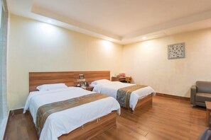 A hotel room with two single beds, wooden flooring, a desk, and a chair.