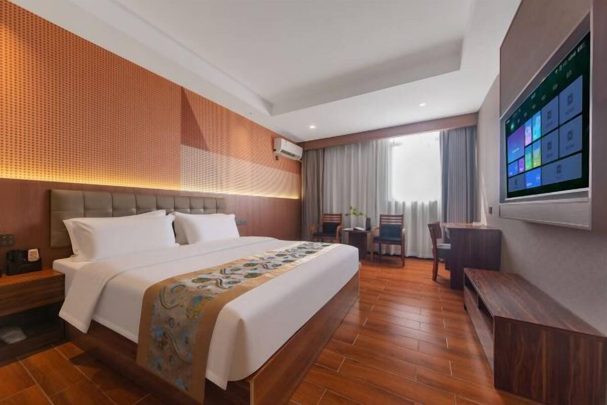Habitación de hotel con una cama grande, un escritorio, una silla, un televisor y una ventana con cortinas.