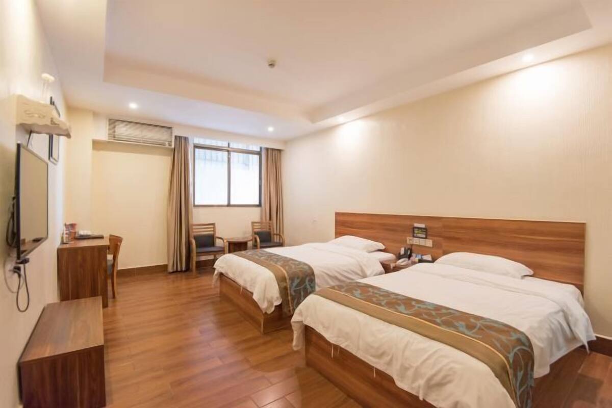 Habitación de hotel con dos camas, un escritorio, una silla y un televisor.