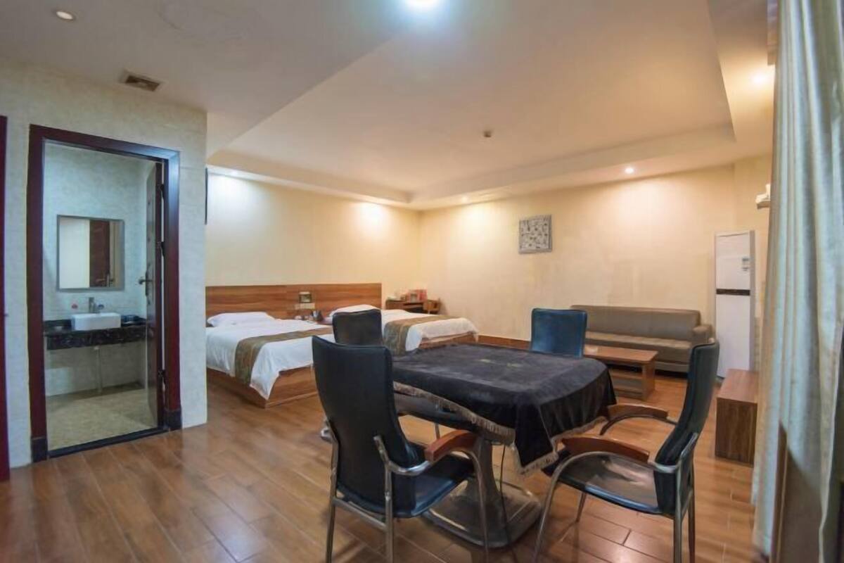Habitación de hotel con cama, sofá, mesa de comedor con sillas, kitchenette y baño con espejo.