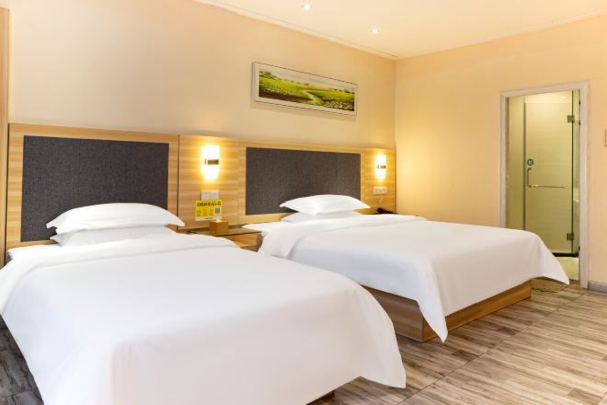 Habitación de hotel con dos camas, cabeceros de madera y lámparas fijadas a la pared.