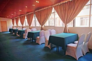 Un salón de conferencias con mesas y sillas, amplias ventanas con cortinas y suelo alfombrado.