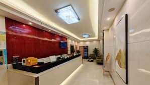 A hotel reception area with a reception desk, a red wall, a television, and a framed artwork on the wall.