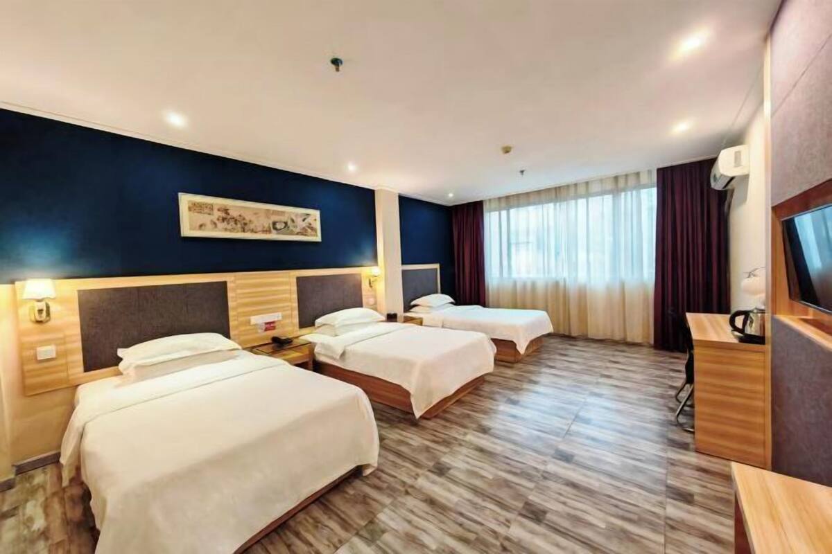 A hotel room with three single beds, a desk, a TV, and a painting on the wall.