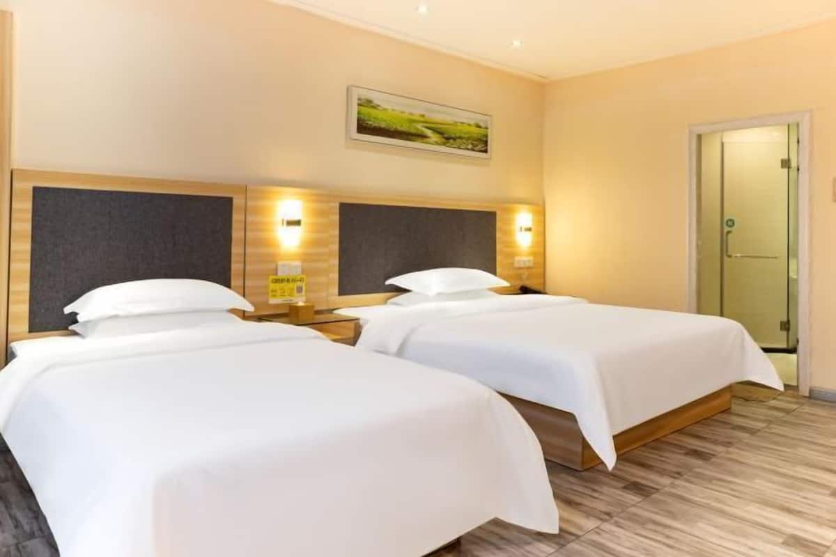 A hotel room with two beds, wooden headboards, and wall-mounted lights.