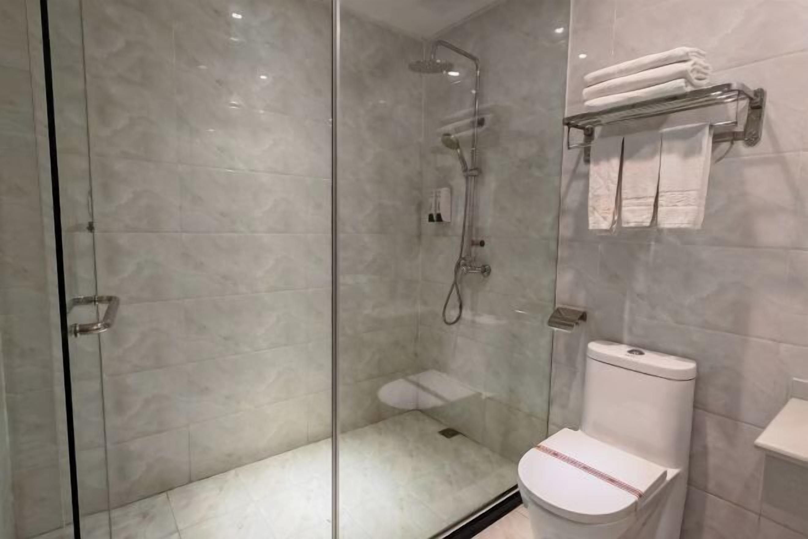 Ein modernes Badezimmer mit einer gläsernen Duschkabine, einer weißen Toilette und einem Handtuchhalter mit gefalteten Handtüchern.
