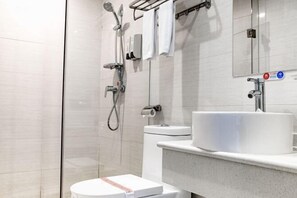Un baño moderno con cabina de ducha de vidrio, inodoro y lavamanos con toallero encima.