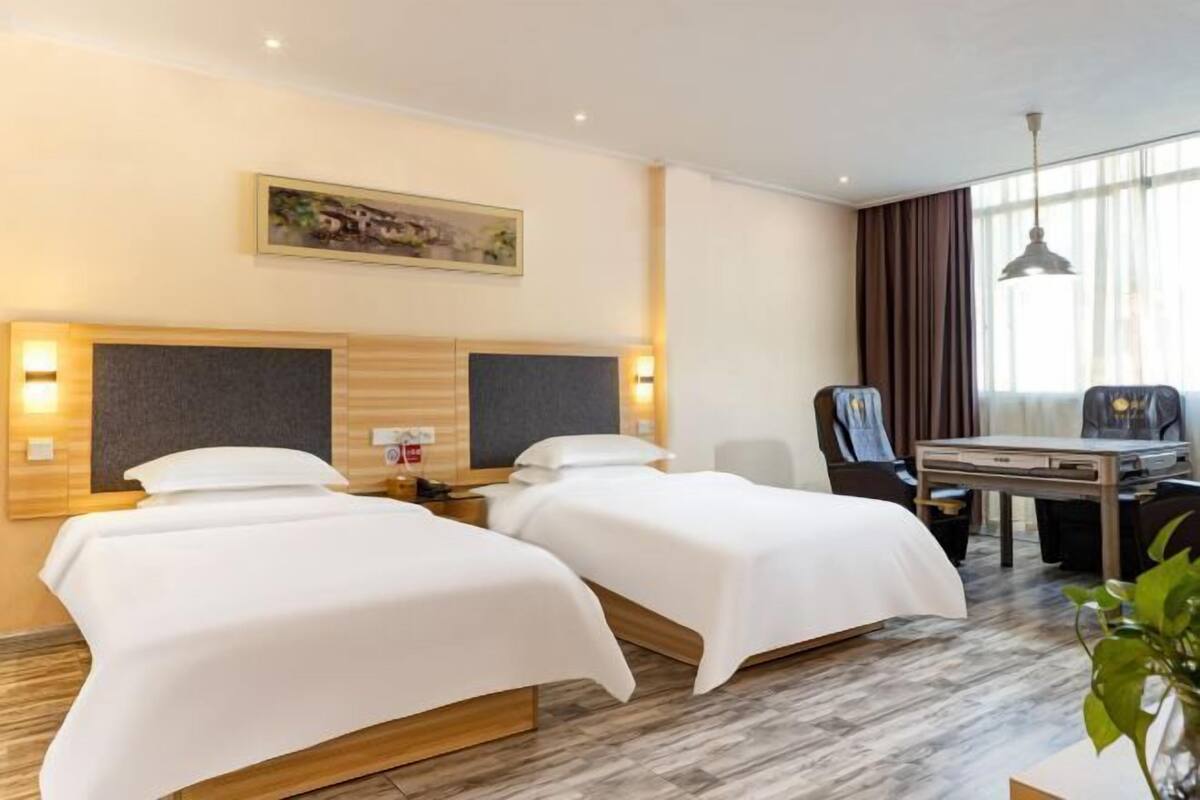 A hotel room with two beds, a desk, a chair, and a large window with curtains.