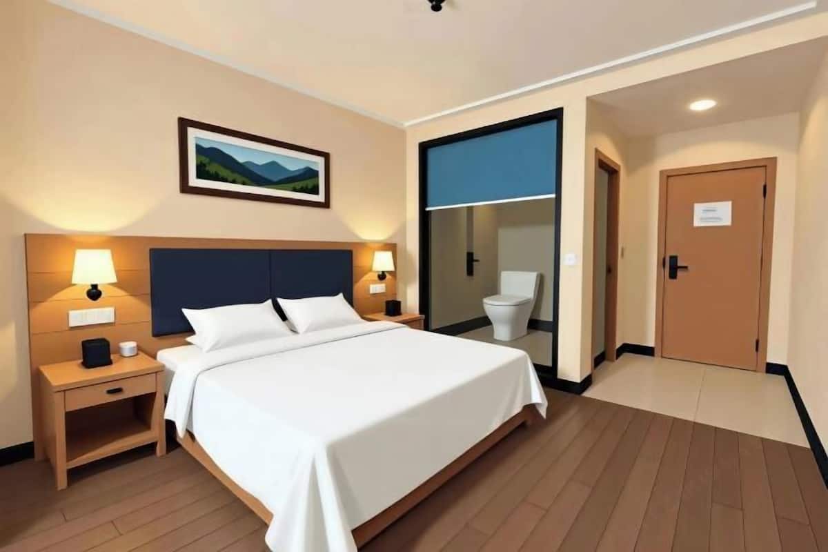 A hotel room with a large bed, bedside lamps, a framed picture on the wall, and a door leading to the bathroom.