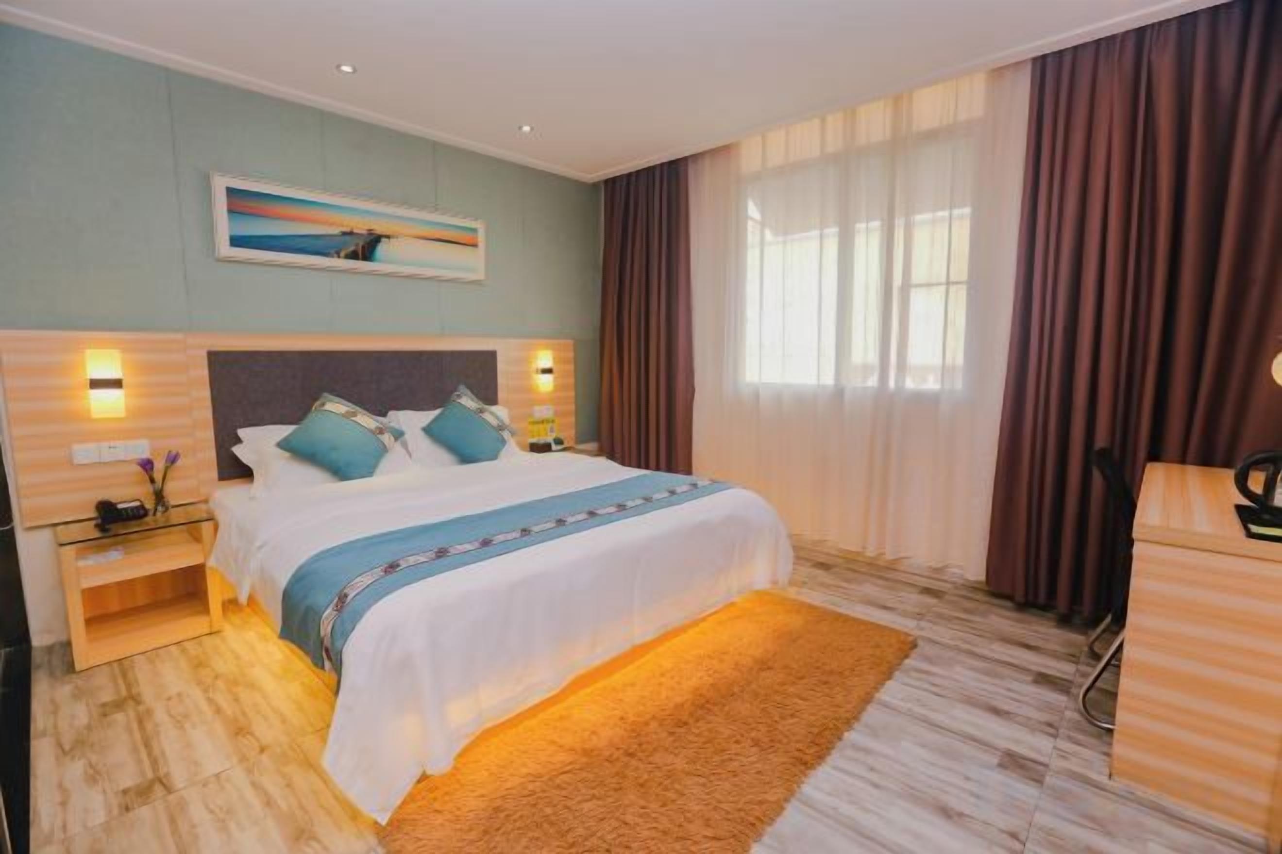 Ein Hotelzimmer mit einem großen Bett, einem Nachttisch, einer Lampe, einem Fenster mit Vorhängen und einem Gemälde an der Wand.