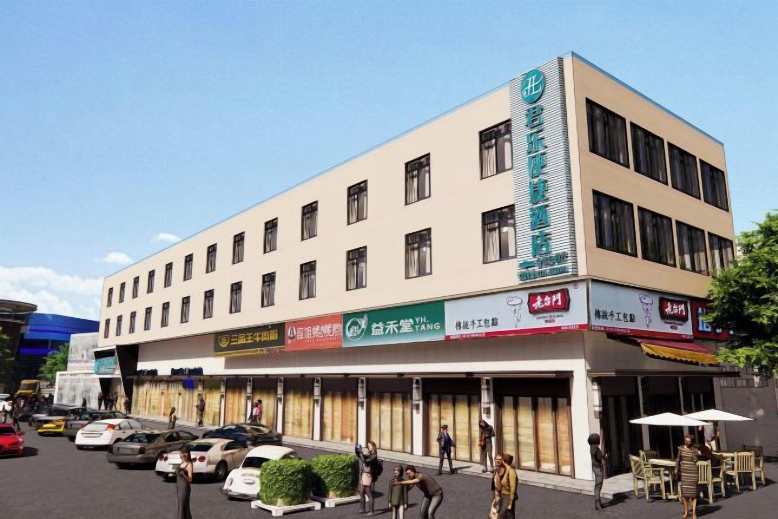 Ein mehrstöckiges Hotel mit schlichter Fassade, mehreren Geschäften im Erdgeschoss und einem Parkplatz mit Autos.