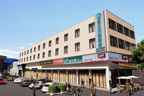 A multi-story hotel with a flat facade, several ground-level shops, and a parking area with cars. - Jungle Express Hotel (Nanning)