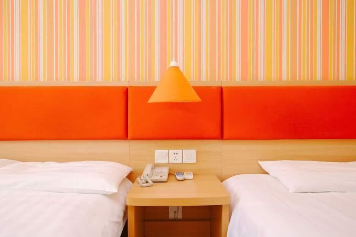 A hotel room with two beds, a wooden nightstand with a telephone and a remote control, and a striped wall with orange and yellow tones.