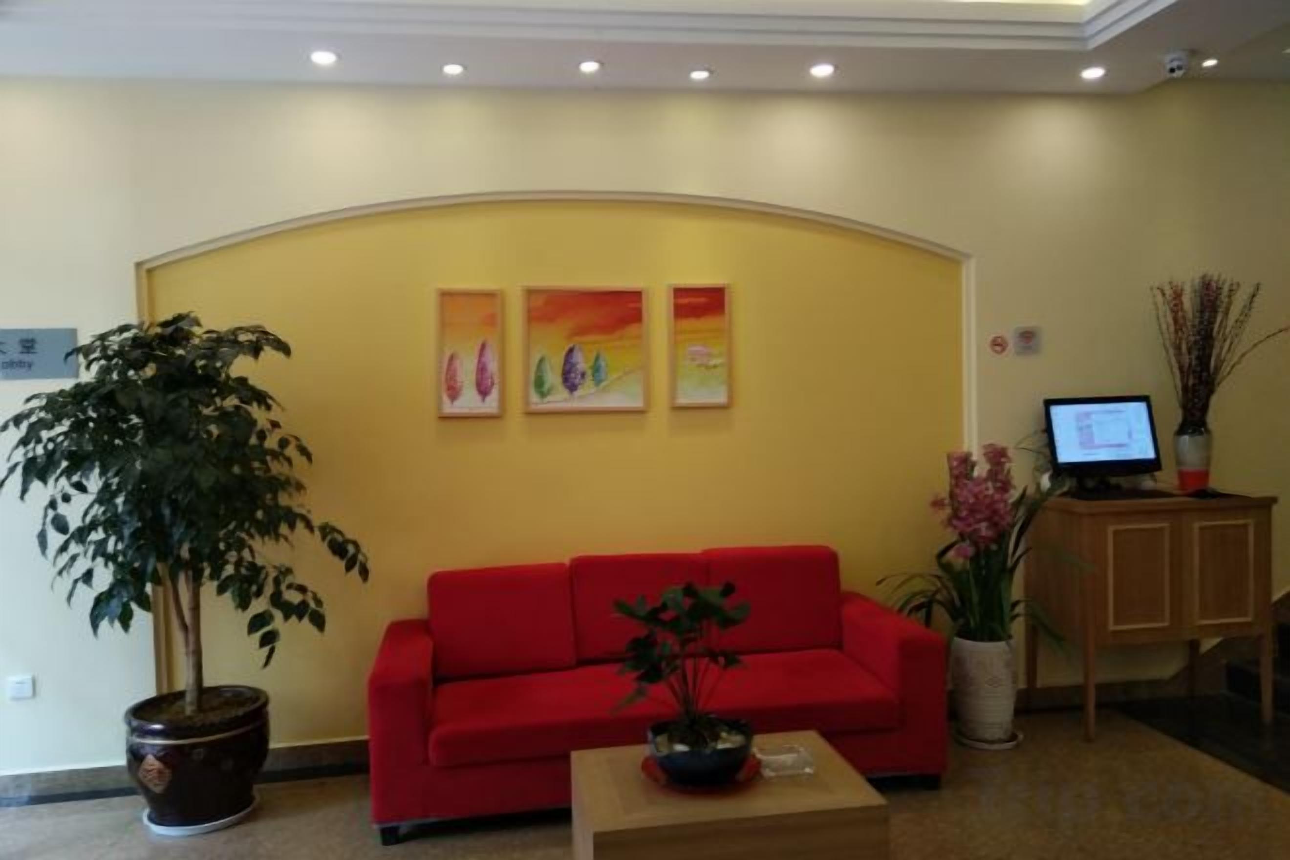 A reception area with a red sofa, a potted plant, and a computer on a desk.