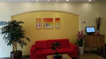 A reception area with a red sofa, a potted plant, and a computer on a desk.