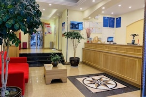 Zona de recepción de un hotel con mostrador, un área de estar rojo, una planta en maceta y un diseño de piso decorativo grande.