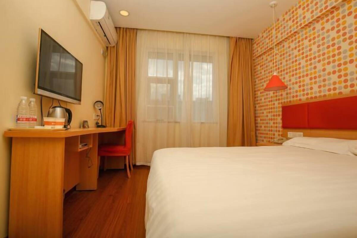 A hotel room with a bed, a desk with a chair, a television, and a window with curtains.