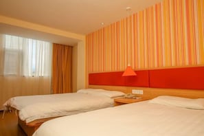 Ett hotellrum med två sängar, en sänggavel i trä, en randig vägg och ett fönster med gardiner.