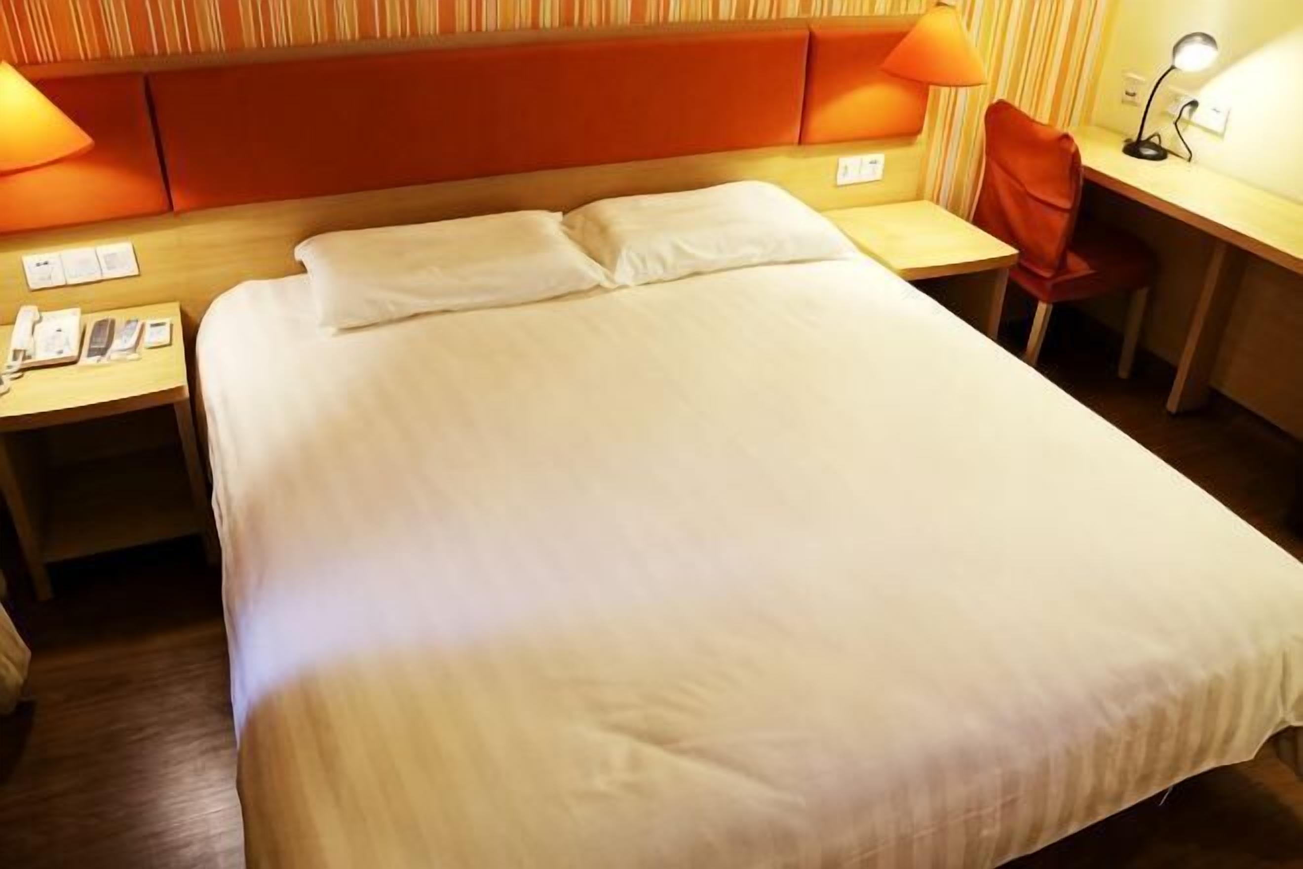 A hotel room with a large bed, a desk, a chair, and a lamp.