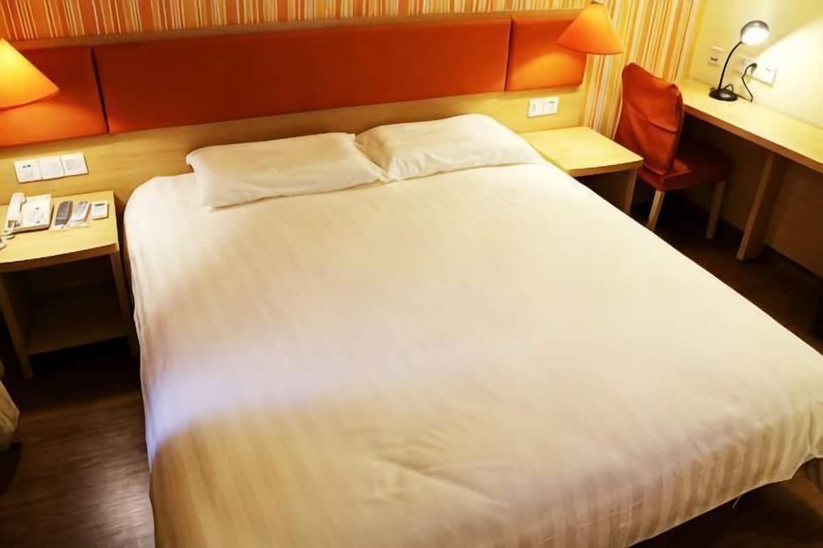 A hotel room with a large bed, a desk, a chair, and a lamp.