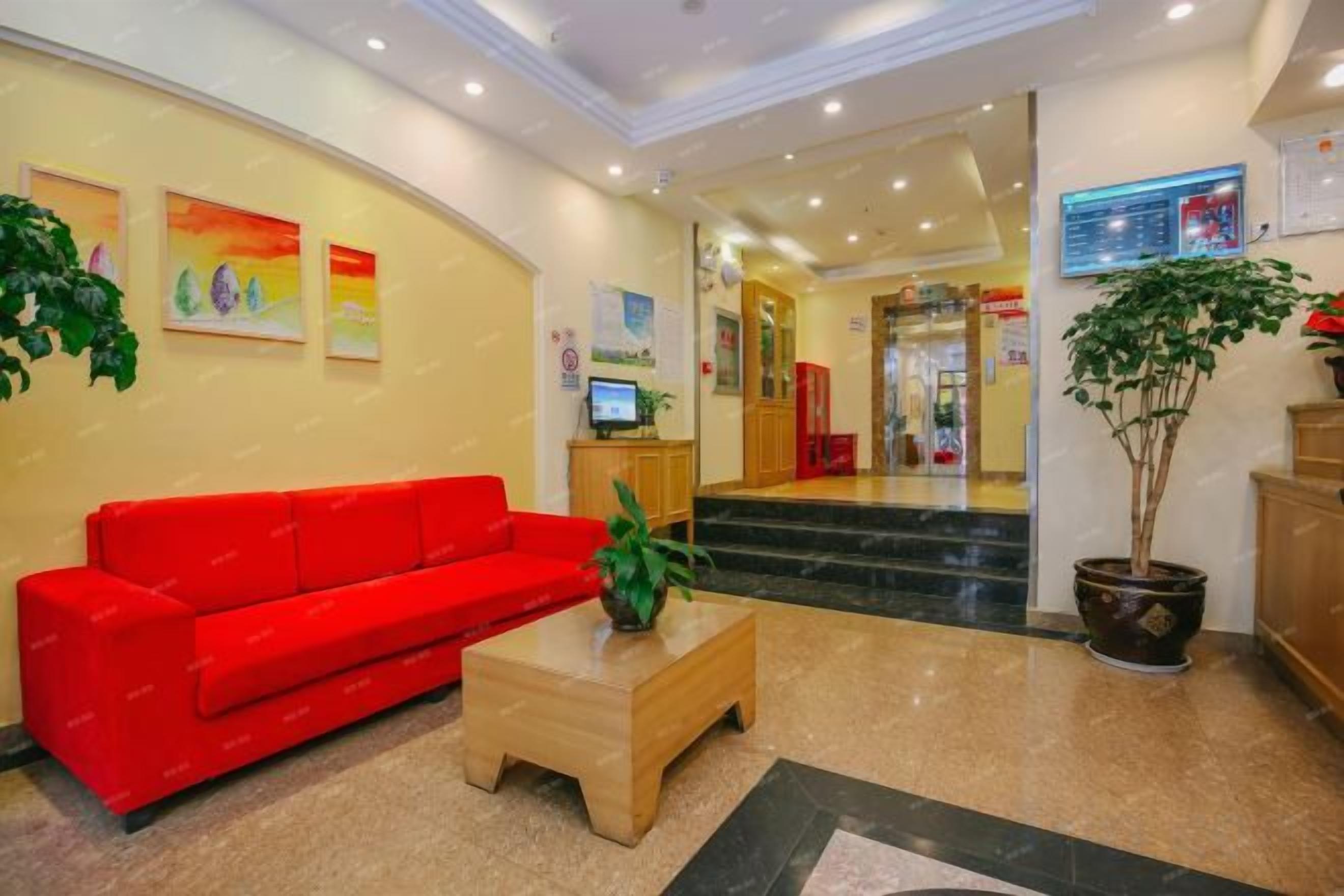 A hotel lobby with a red sofa, a wooden coffee table, a potted plant, and a reception desk.