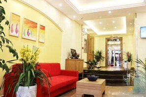 Una hall d'hotel con un divano rosso, una reception e una scala che conduce ai piani superiori.