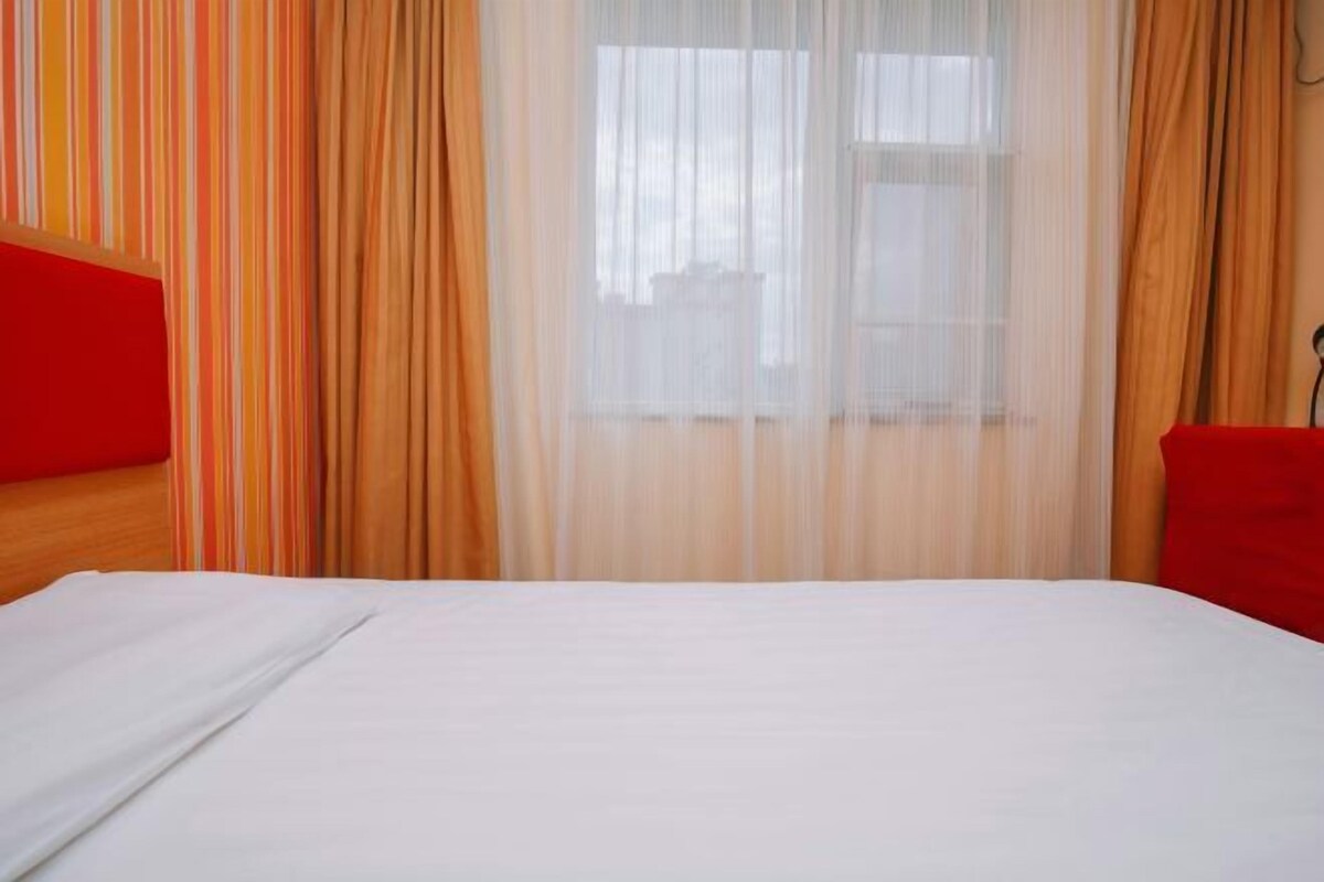 A hotel room with a bed, curtains, and a window.