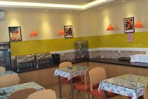 Interior de restaurante com mesas, cadeiras e balcão com alimentos expostos.