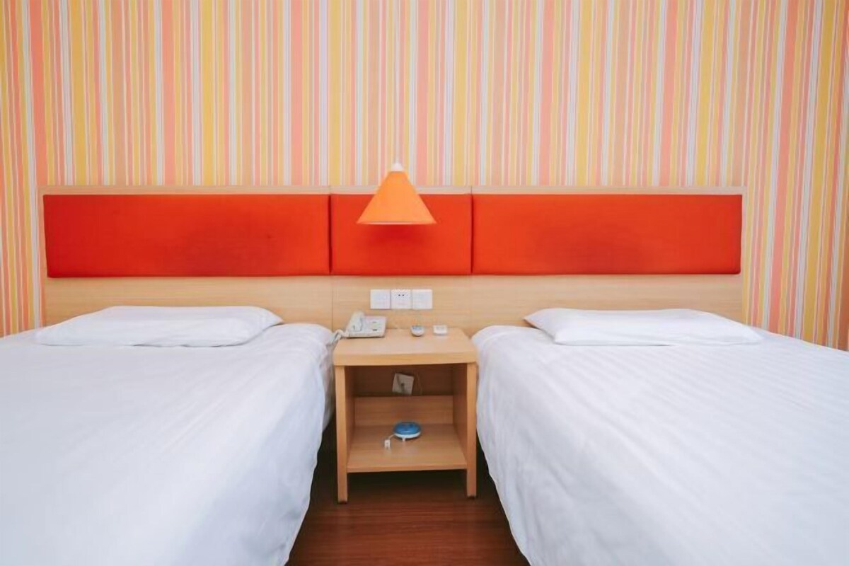 A hotel room with two beds, a wooden nightstand, a red accent wall, and a striped wallpaper background.