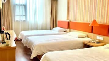 A hotel room with two single beds, a wooden nightstand with a phone, a coffee maker, and a window with curtains.