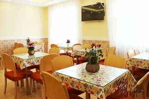 Un comedor con varias mesas y sillas, cada una con mantel de flores. Algunas mesas tienen plantas en macetas.