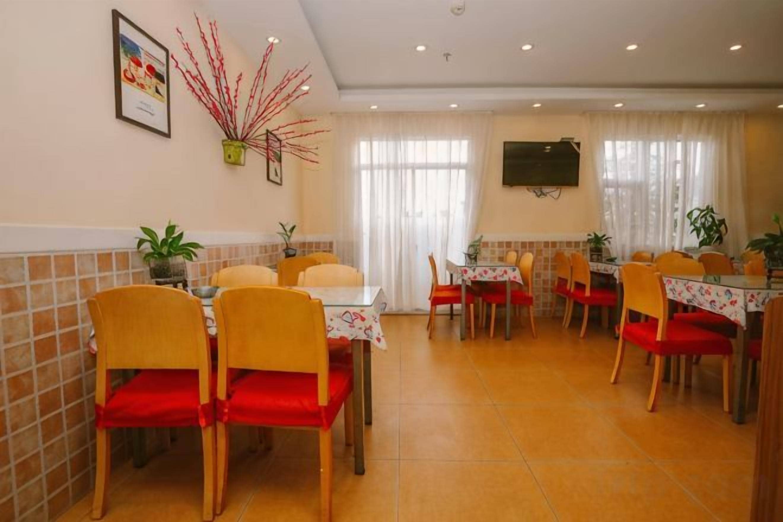 A dining area with multiple tables and chairs, a television mounted on the wall, and a plant on the wall.