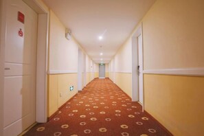 Un corridoio d'hotel con pavimento tappezzato, porte su entrambi i lati e una parete di colore chiaro.