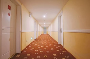 Un pasillo de hotel con piso alfombrado, puertas a ambos lados y pared de color claro.