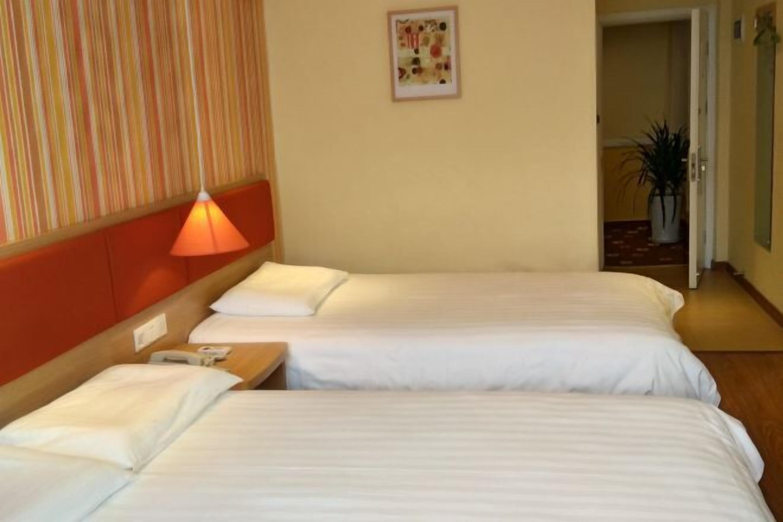 Een hotelkamer met twee bedden, een nachtkastje met een lamp en een lijst aan de muur.