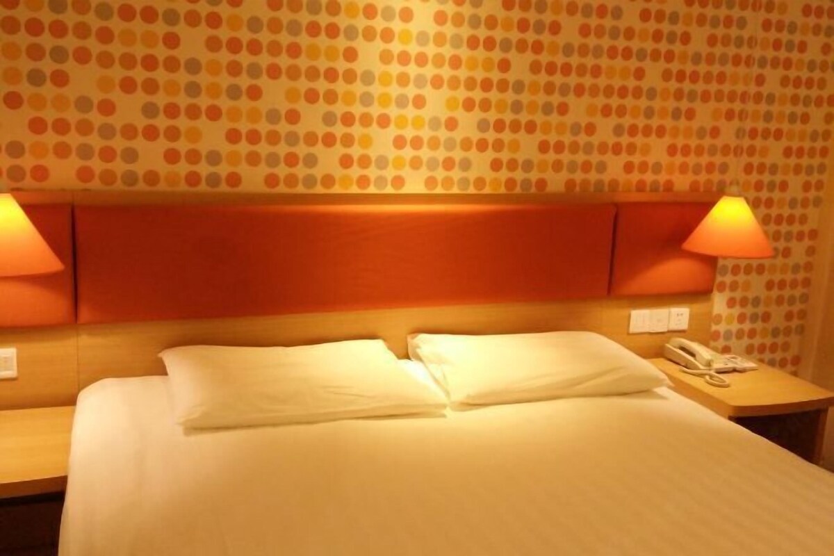 A hotel room with a bed, two bedside lamps, a telephone, and a wall with a polka dot pattern.