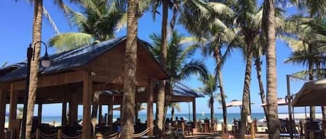 Un restaurante frente al mar con terraza, palmeras y vistas al océano.