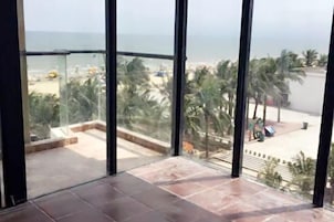 A room with a large glass window overlooking a beach and palm trees.