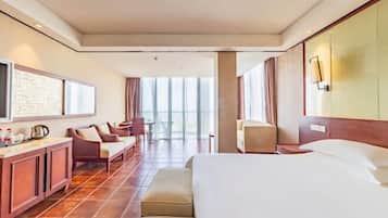 Habitación de hotel con una cama grande, zona de estar con sofá y sillones, una mesita, minibar y un ventanal con cortinas.