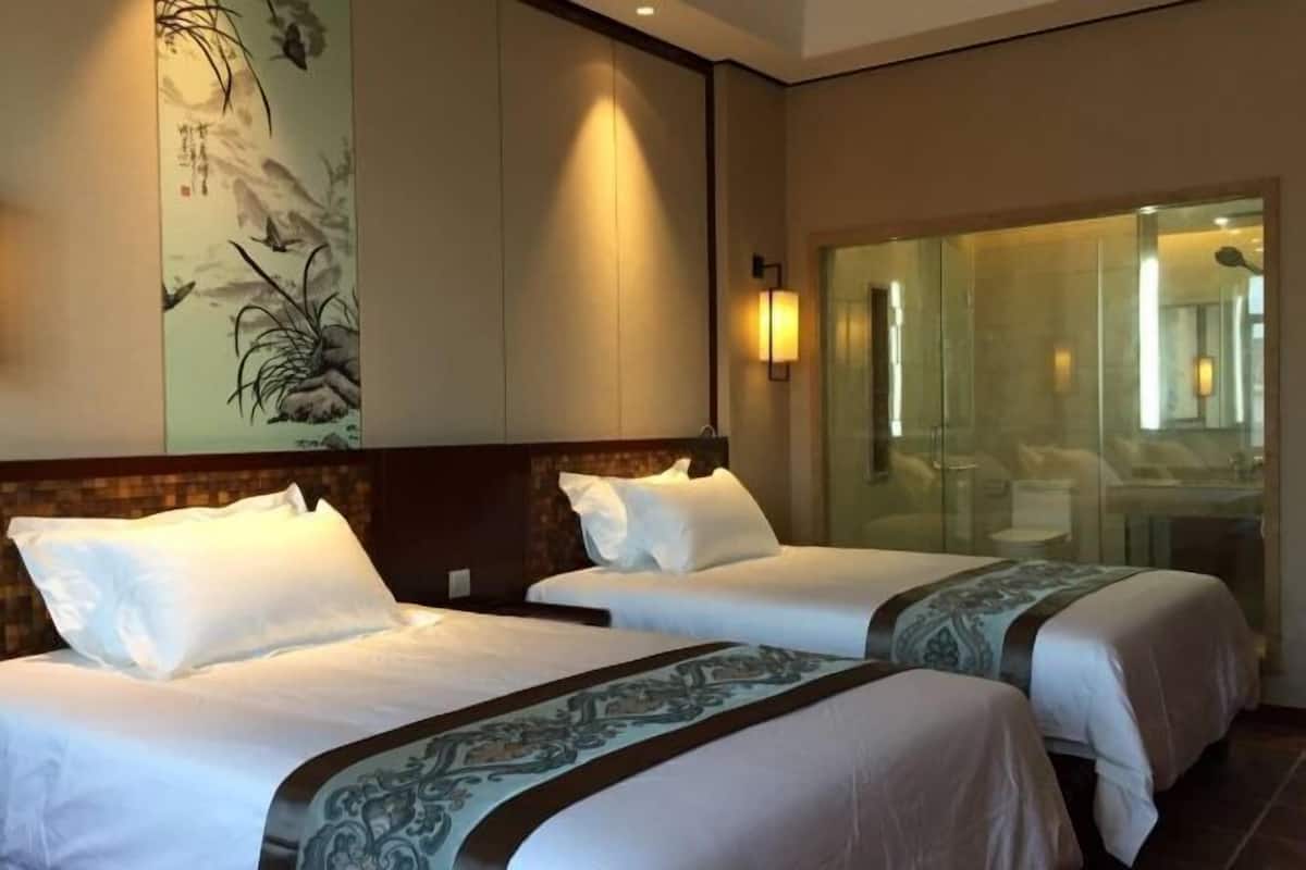 Hotellihuone, jossa on kaksi sänkyä, suuri seinämaalaus ja lasinen suihkukaappi.