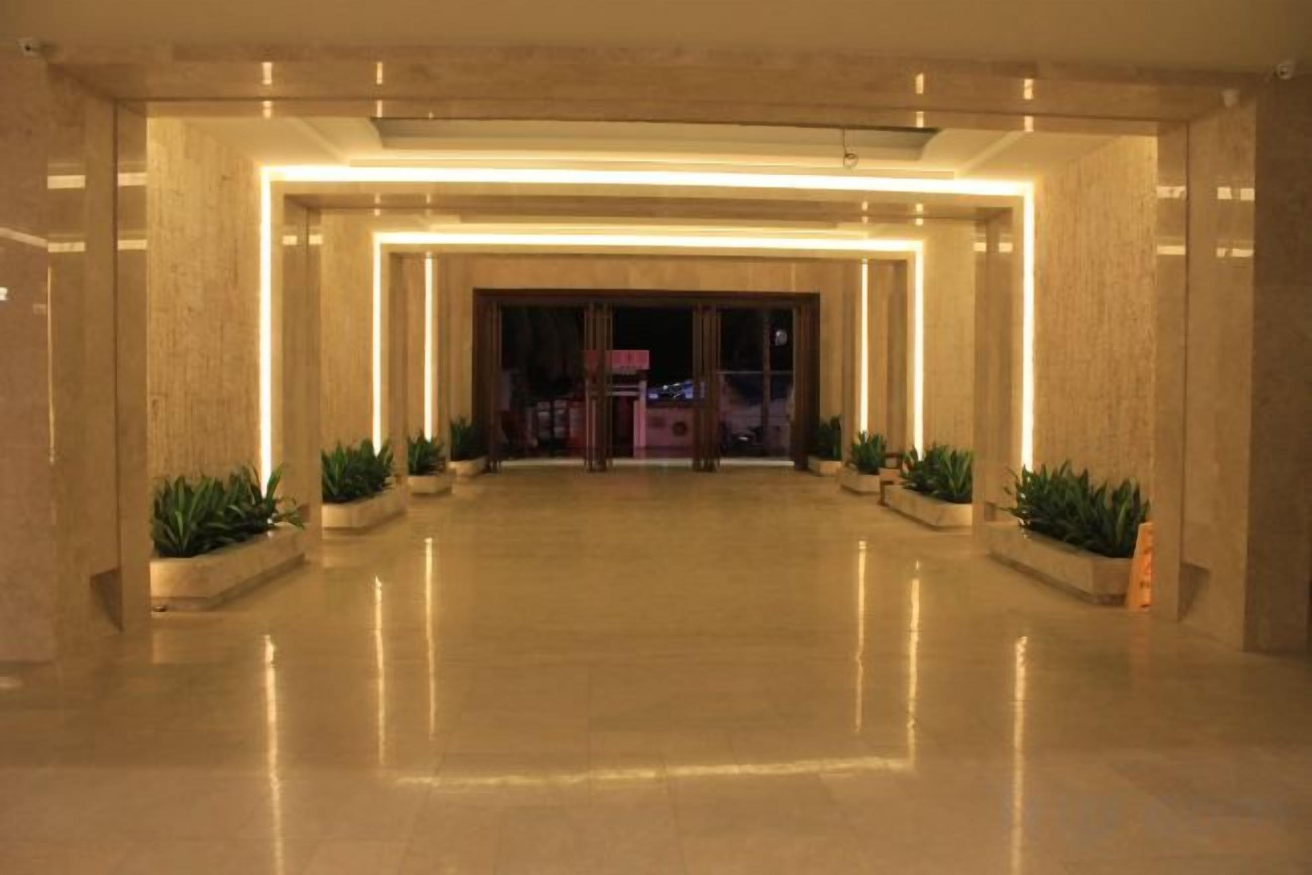 A spacious lobby with a polished floor, a central entrance, and potted plants.