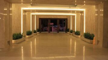 A spacious lobby with a polished floor, a central entrance, and potted plants.